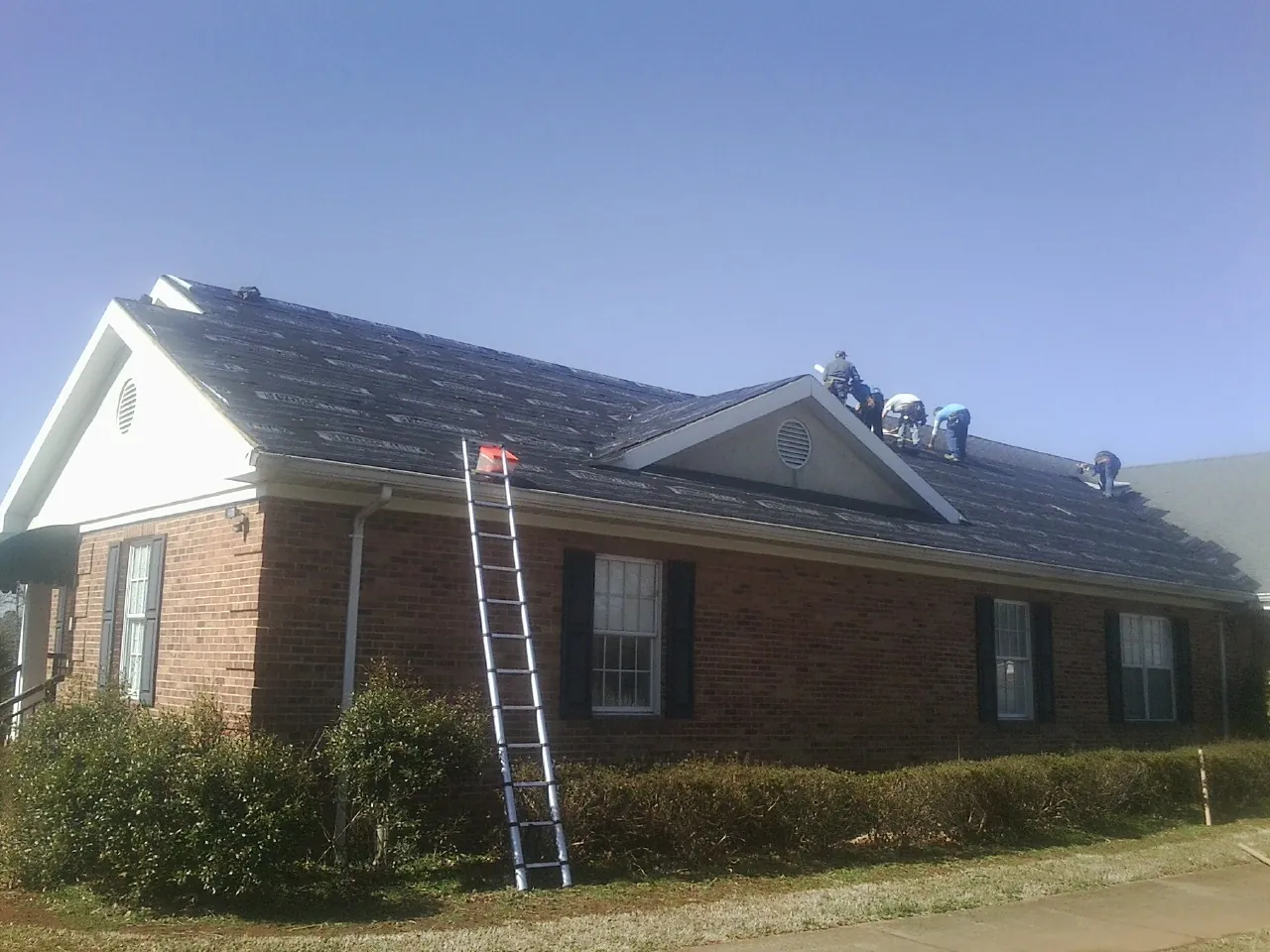 Crew tearing shingles off a brick ranch roof with a ladder set — Metal Roof Repair work by our crew in Catlett