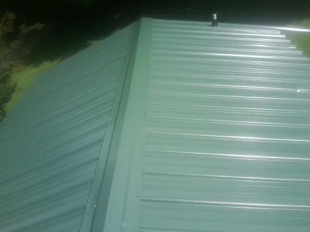 New green metal panels meeting at the ridge of a roof — Flat Roof Repair work by our crew in Catlett