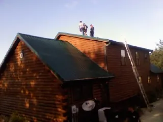 Crew on the ridge of a green metal roof on a two story log home in Catlett