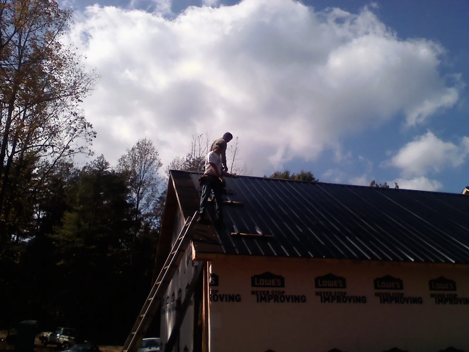 Roofer fastening dark metal panels high against a cloudy sky, from a Roof Inspection job in Catlett