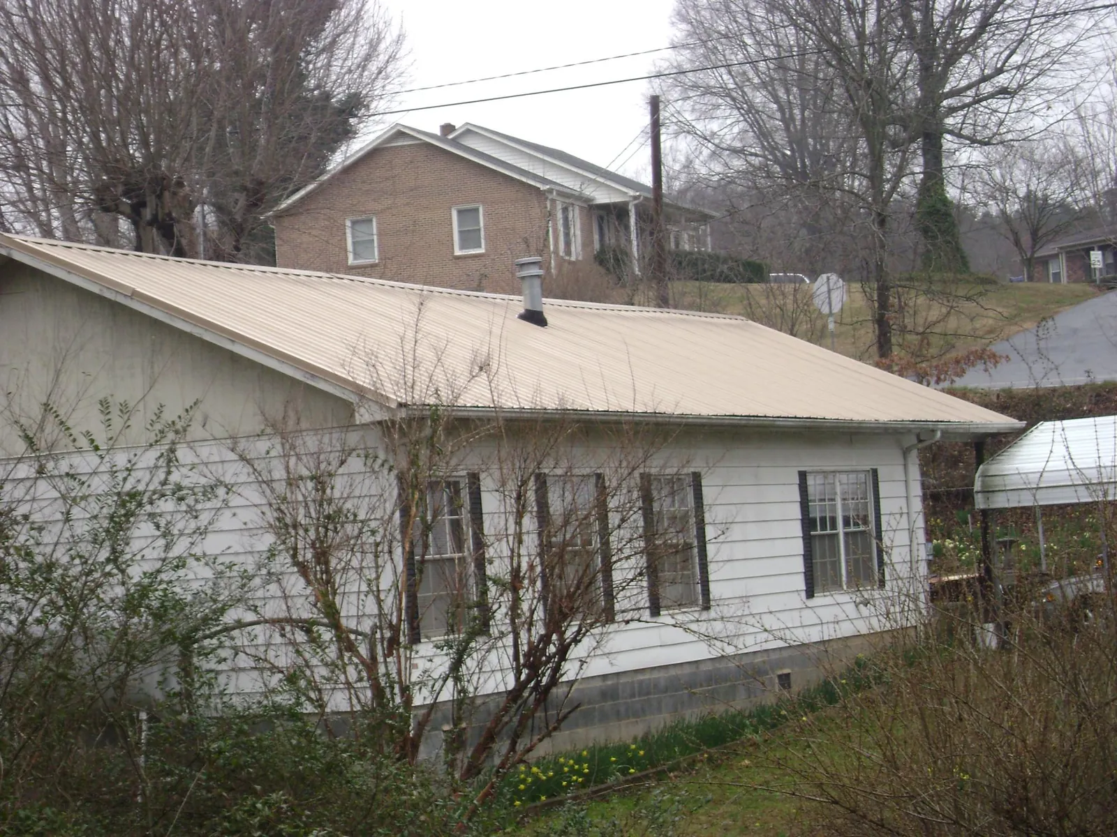 Tan metal roof on a white sided house set into a hillside — Commercial Roofing by Roofing Brothers in Catlett